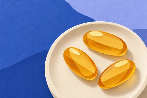 Paper collage of three golden softgels on a cream dish against blue