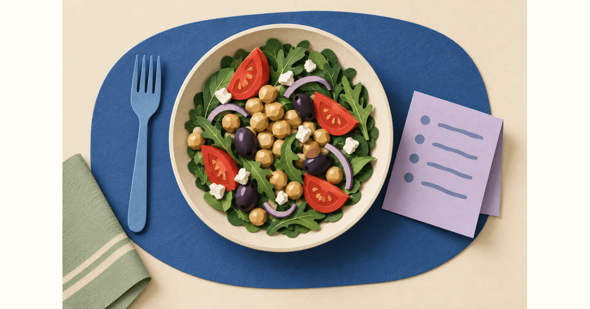 Paper collage of a Mediterranean bowl with chickpeas, tomatoes, greens and olives beside a blue fork and a lavender meal-plan card